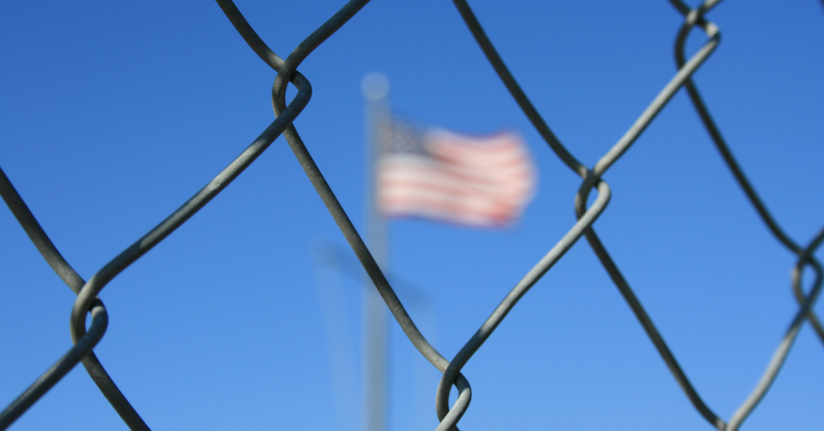 American Flag behind a chain link fence/ chinese migrants at the us border